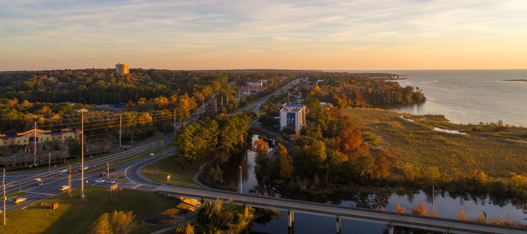 Aerial view of Daphne, Alabama showing a scenic highway, wooded areas, and coastal waters at sunset