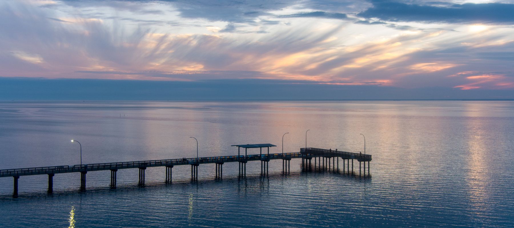 A peaceful pier stretches into calm bay waters at dusk in Fairhope, Alabama, under a dramatic sky