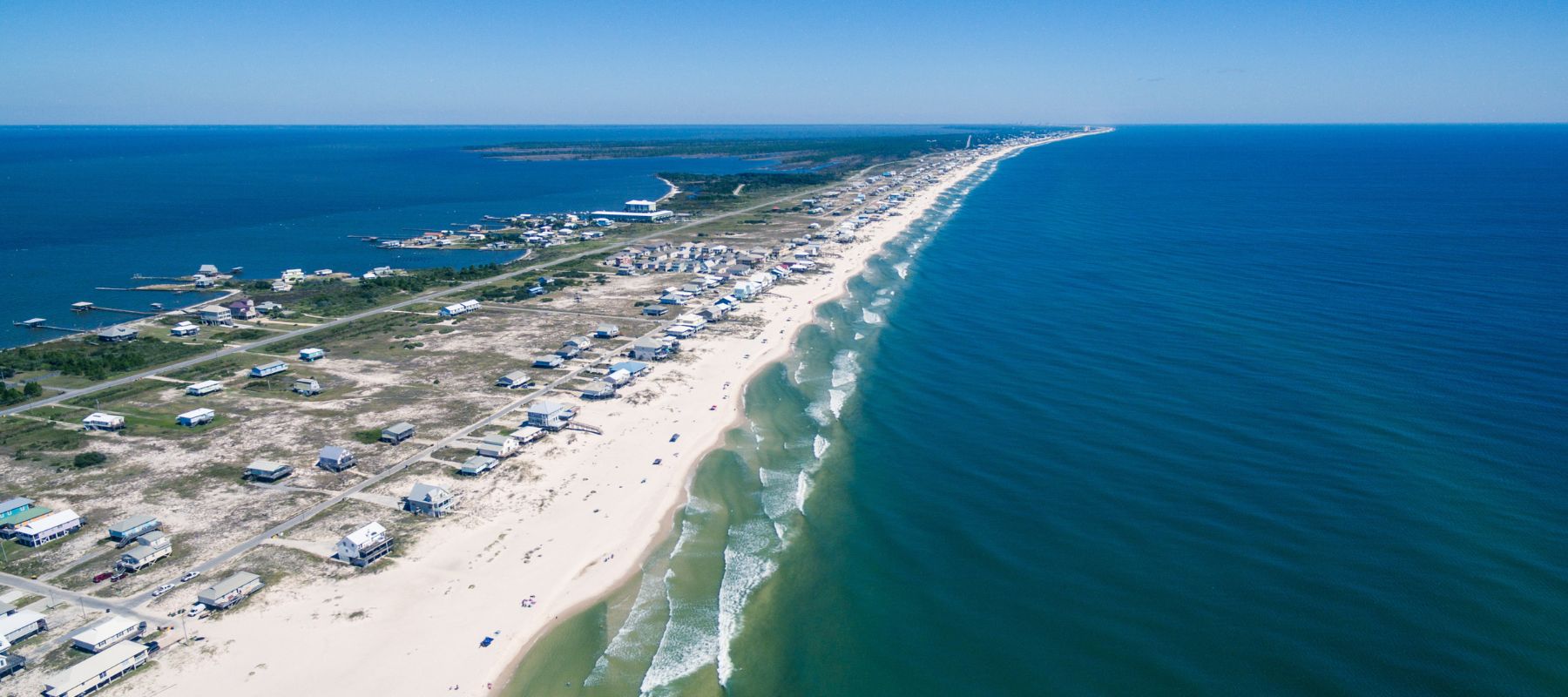Panoramic aerial of Gulf Shores, Alabama, featuring a long stretch of beachfront homes and turquoise ocean