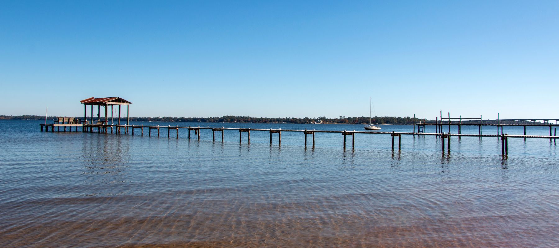 Quiet lakeside dock with a wooden canopy and a moored sailboat on the calm waters of Lillian, Alabama
